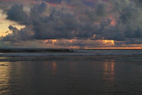 Lone surfer riding wave under dramatic stormy sky at dusk,