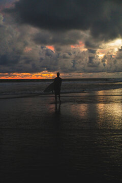 Surfer silhouette standing on beach gazing at stormy horizon, Bali