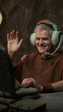 Happy businessman wearing a headset and having a video call on his laptop, he is smiling and waving at the screen: technology in the stone age concept