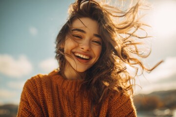 Fototapeta premium Happy young woman smiling joyfully with flowing hair, looking down at the camera from a unique angle in vibrant cozy knit sweater outdoors.
