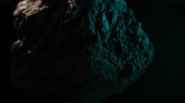 Close-up dark rock surface with green light and rugged texture