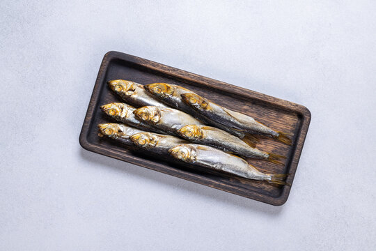 Smoked capelin herring fish on dark wooden tray