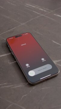 Vertical Screen: A smartphone displays an incoming call marked as spam. It rests on a table, highlighting the issue of unwanted calls and the need for detection strategies.