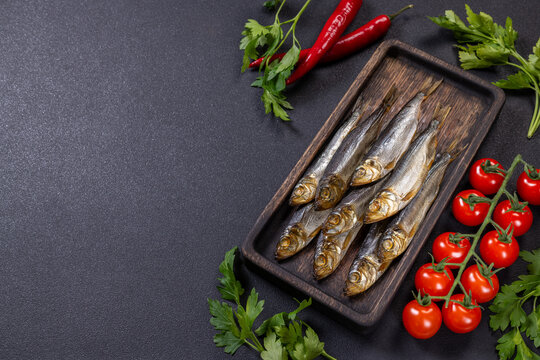 Smoked capelin herring on cutting board with fresh vegetables