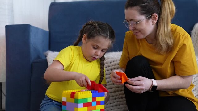 Mother and daughter build block tower on couch while child arranges colorful toy brick and parent guides play and learning in family living room with focused attention and joyful interaction
