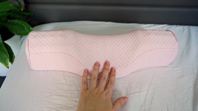 Point of view touching ergonomic orthopedic pillow on bed. Feeling soft memory foam texture, checking comfort and shape for cervical support, neck alignment and better sleep at home.
