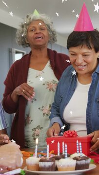 Vertical video: Honoree gift leaning to cakes as hand lighting candles, animated stars for birthday