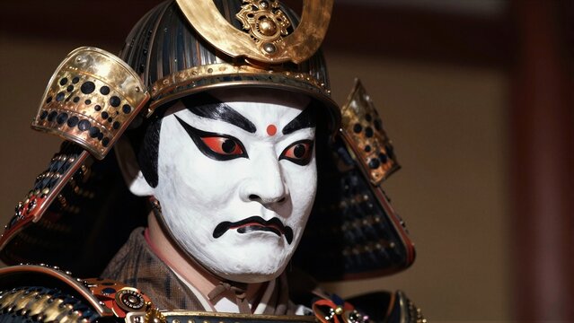 Close-up of a Japanese Noh theater actor in elaborate samurai armor and white face paint with red eyes, under dramatic stage lighting.