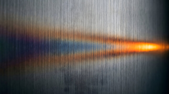 Abstract brushed metal background featuring a glowing orange light streak with prismatic diffraction effects on a textured stainless steel surface.