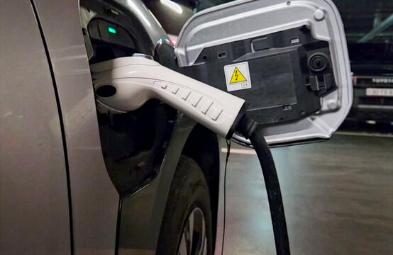 Electric Vehicle Charging at Underground Parking Station. Close-up of a white charging cable plugged into an electric car in a dimly lit underground parking garage. Concept of eco-friendly transport