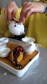 Traditional chinese tea ceremony gongfu cha with white ceramic teapot, cups and golden money frog on bamboo tray. Pouring oolong tea, mindful atmosphere, oriental culture and zen lifestyle.