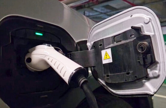 Electric Vehicle Charging at Underground Parking Station. Close-up of a white charging cable plugged into an electric car in a dimly lit underground parking garage. Concept of eco-friendly transport