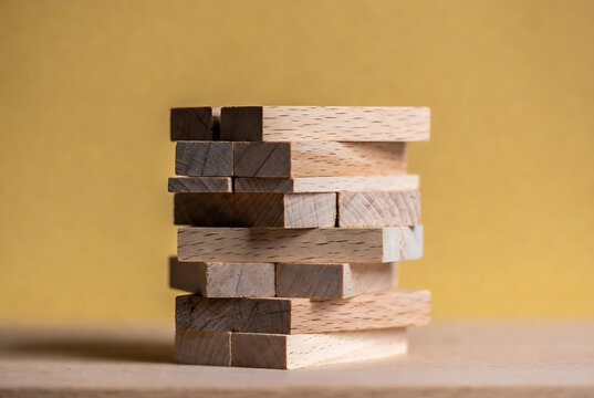 A stack of wooden blocks rests on a table against a yellow background.