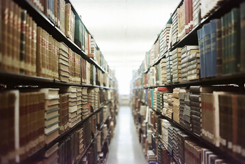 Fototapeta premium A long row of bookshelves filled with books stretches into the distance, creating a tunnel-like effect.