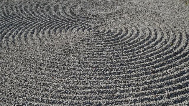 A detailed close-up of a Karesansui dry garden. Sunlight highlights the intricate circular raked gravel patterns and ripples in the white sand, creating a meditative and peaceful atmosphere.