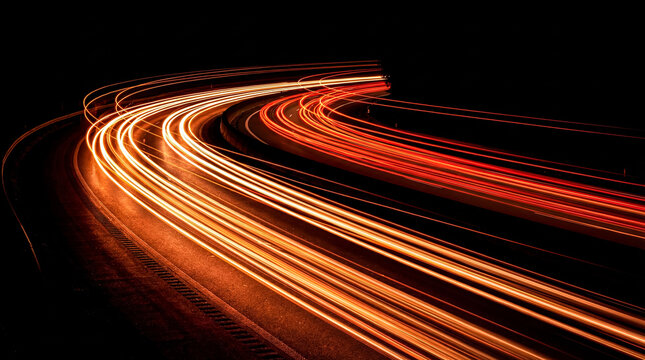 Long exposure photograph capturing bright car light trails on a curved highway.