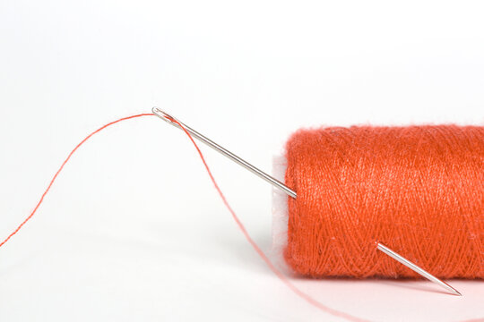 Sewing needle with red thread through the white background