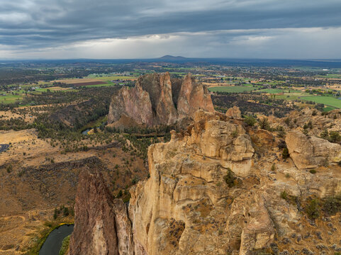Aerial view of Smith Rock State Park featuring towering basalt cliffs, the winding Crooked River, and distant farmland under a dramatic sky in Crooked River, Oregon, United States.