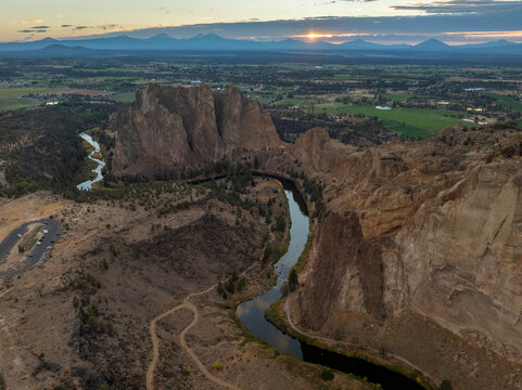 Aerial view of Smith Rock State Park featuring the winding Crooked River, towering basalt cliffs, and a sunset over distant mountains in CROOKED RIVER, Oregon, United States.