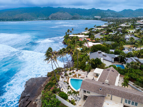 Aerial view of turquoise waters crashing against the rugged coastline, meeting lush green landscapes and elegant homes, Honolulu, Hawaii, United States.