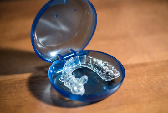 A clear aligner in a blue case rests on a wooden surface. It&rsquo;s being presented or displayed.