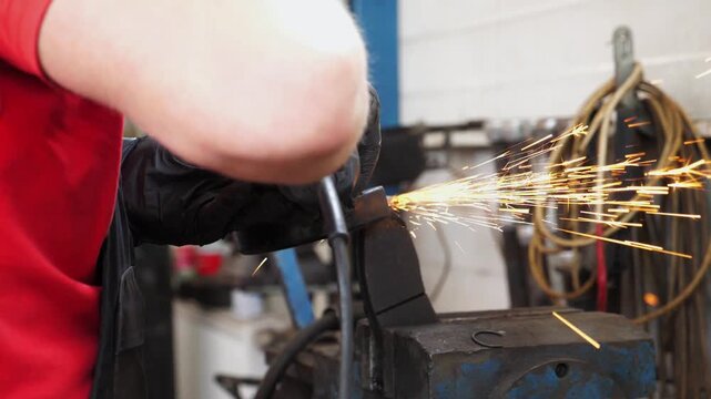 Skilled technician in red shirt and gloves operates a power tool, creating sparks while grinding metal in a garage, showcasing the dynamic process of automotive repair and craftsmanship