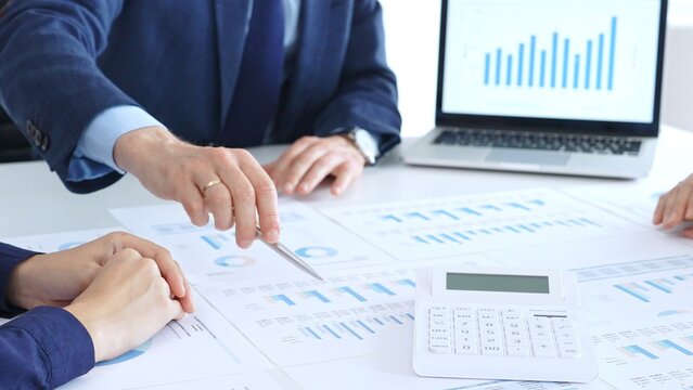 Business people collaborating at a conference table, reviewing financial charts and reports, using a laptop and calculator while engaging in discussions about strategy and performance. Accouters at
