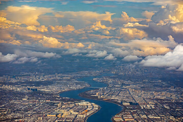 Obraz premium Aerial view of a city skyline with a river winding through it, under a dramatic sky filled with clouds.