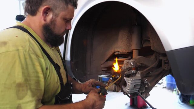Skilled automotive technician using a torch to heat a component during car repair in a garage, showcasing the intricate process of vehicle maintenance and repair techniques
