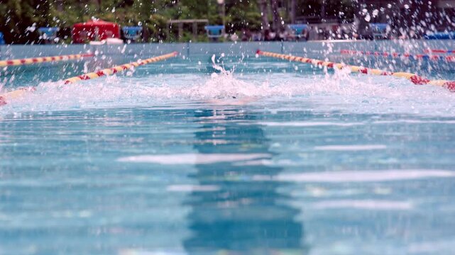 Freestyle stroke in a pool competition. Swimmer in black cap, focused, with water splashing around, separated by colored dividers.