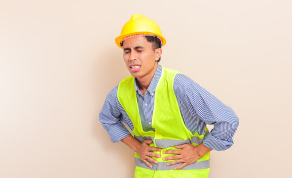 asian construction worker with yellow hard hat and safety vest holding stomach in pain, isolated background, workplace injury concept