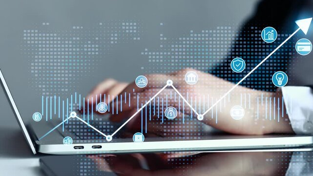 Hands typing on a laptop with financial graphs and icons displayed on the screen in a modern office setting during daytime.