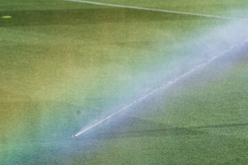 Sprinklers Creating a Rainbow Over a Well-Maintained Football Stadium Pitch with Striped  © minortica7