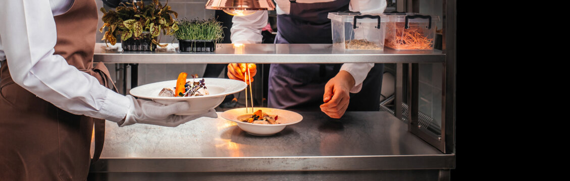 Chef plating gourmet dish and waiter serving in professional restaurant kitchen