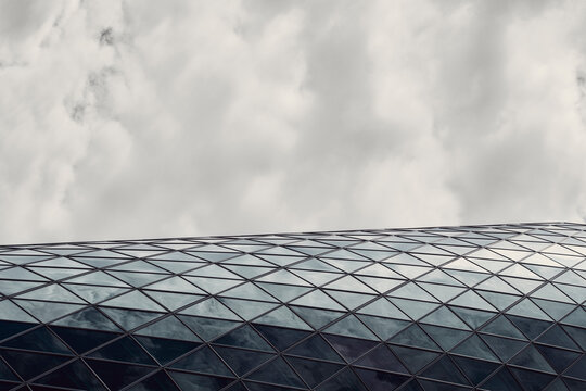 Modern curved glass roof and facade pattern in architecture framed by sky clouds leaving generous copyspace for minimal editorial compositions