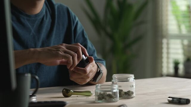 Man using cannabis grinder, with cannabis equipment and accessories on the table.
