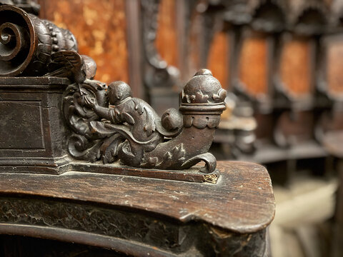 CAPUA, ITALY - NOV 2025: Close-up of a wood-carved armrest in the choir stalls at the Church of Saint Mary of the Announcement, featuring a putto riding a mythical creature. 2/4