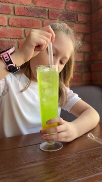 A schoolgirl in a cafe-restaurant is drinking lemonade with ice and tapioca balls.
