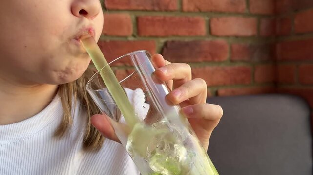 A schoolgirl in a cafe-restaurant is drinking lemonade with ice and tapioca balls.
