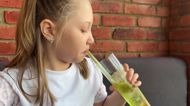 A schoolgirl in a cafe-restaurant is drinking lemonade with ice and tapioca balls.
