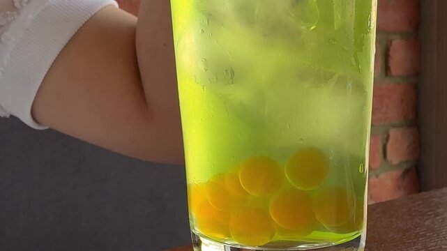 A schoolgirl in a cafe-restaurant is drinking lemonade with ice and tapioca balls.
