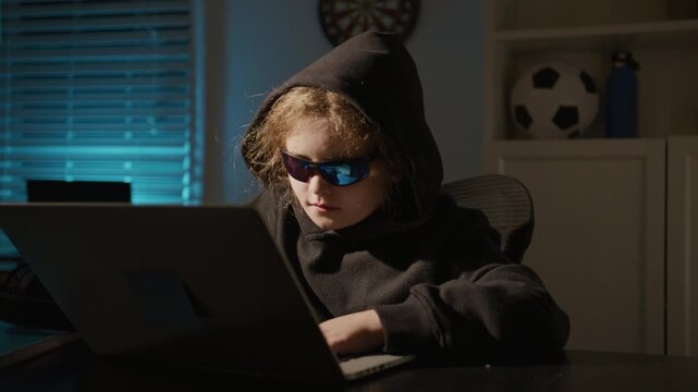 Hacker kid hack private information. Hacker child typing malware code. Dark hack kid activity. IT hacker child online attack. Hacker kid typing code in laptop at night office.