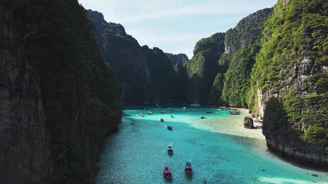 Stunning aerial perspective of traditional Thai long tail boats floating on turquoise waters in Maya Bay, surrounded by limestone cliffs.