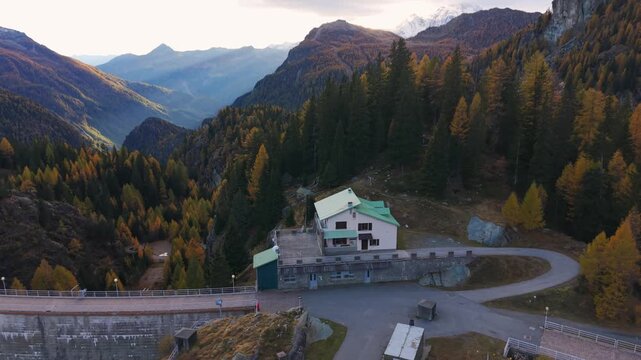 Campo Moro dam and building, surrounded by autumn forests in Italian Alps, Valmalenco, Italy. Aerial tilt-down forward