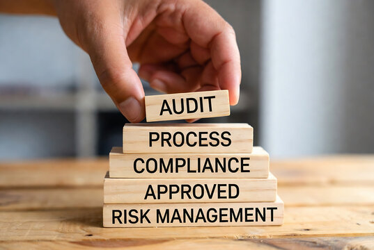 A hand holding a stack of wooden blocks displaying an audit process compliance and risk management sequence.