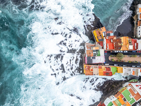 Aerial view photo from above wild waves in the Atlantic Ocean with colorful houses on Tenerife island in Puerto de la Cruz, Spain