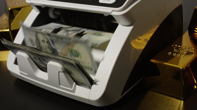Money counting machine processing dollar bills. Cash count in motion. Gold bars and US dollars. Cash counting action. Counting machine for finance theme. Golden bars with rotating dollar bills.