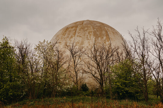 Concrete Spherical Dome Towering Above Trees, Ruststreaked Surface And Weathered Panels Evoking Postindustrial