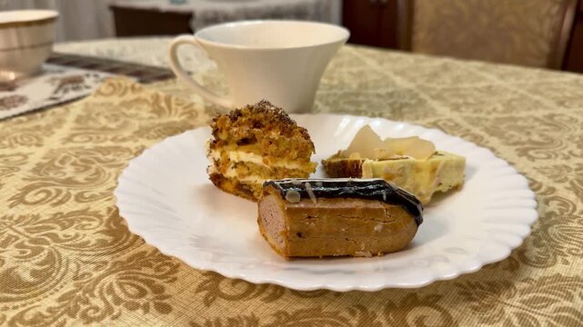 Plate with coffee and pastries on table, white plate featuring chocolate eclair and cake pieces next to porcelain mug, ornate gold.