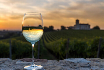 Naklejka premium A wine glass reflects a vineyard and sunset landscape with a castle in the distance. It’s a moment of relaxation and enjoyment amidst beautiful scenery.